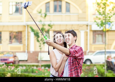 Heureux les jeunes touristes de prendre un couple sur le smartphone avec selfies monopied en ville. L'homme est maintenant le stick et le tir à la recherche au téléphone avec ha Banque D'Images