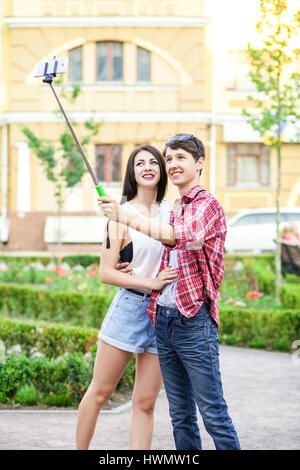 Heureux les jeunes touristes de prendre un couple sur le smartphone avec selfies monopied en ville. L'homme est maintenant le stick et le tir à la recherche au téléphone avec ha Banque D'Images