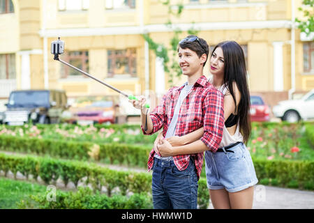 Heureux les jeunes touristes de prendre un couple sur le smartphone avec selfies monopied en ville. L'homme est maintenant le stick et le tir à la recherche au téléphone avec ha Banque D'Images