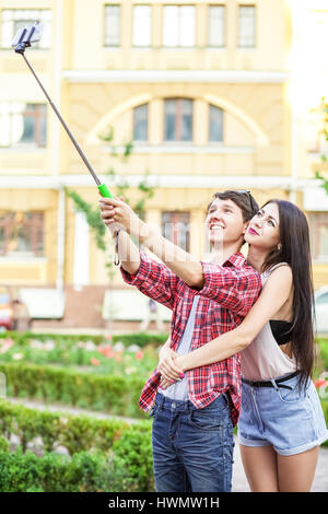 Heureux les jeunes touristes de prendre un couple sur le smartphone avec selfies monopied en ville. L'homme est maintenant le stick et le tir à la recherche au téléphone avec ha Banque D'Images