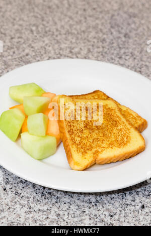 Photographie verticale de pain doré avec des fruits cuits sur plaque blanche placée sur plateau en marbre gris et noir. Espace copie ci-dessus. Simple, repas santé. Banque D'Images