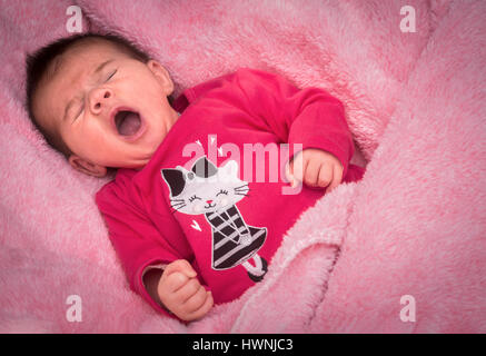 Un bébé nouveau-né fille bailler sur une couverture rose, certainement regarda amoureusement par ses parents qui profitent de la moindre de ses expressions comiques.
