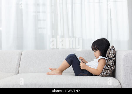 Chinois asiatique petite fille allongée sur le canapé avec tablette dans la salle de séjour à la maison Banque D'Images