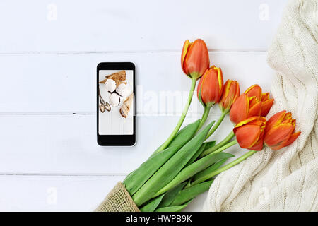 Passage tiré d'un téléphone cellulaire avec photo d'un dessert aux fraises avec un bouquet de tulipes pour la Journée nationale de la crème glacée et d'un tricot confortable jeter couverture sur Banque D'Images