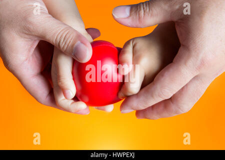 Abstract shot close up hand de père main courante main courante pour enfants cœur rouge sur fond orange Banque D'Images