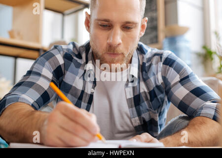 Besoin de le faire. Réfléchis sérieusement porté homme tenant un crayon et dessiner un croquis tout en étant concentré sur son travail Banque D'Images