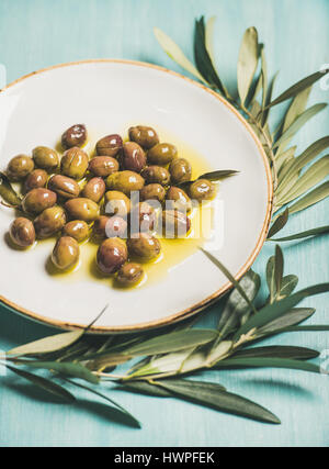Olives marinées dans l'huile et branche d'arbre sur fond bleu Banque D'Images