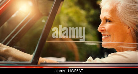 Smiling mature woman driving red cabriolet pendant journée ensoleillée Banque D'Images