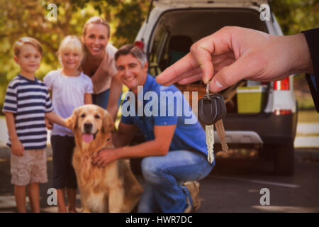 Femme heureuse de recevoir des clés de voiture contre famille avec chien en voiture sur route Banque D'Images