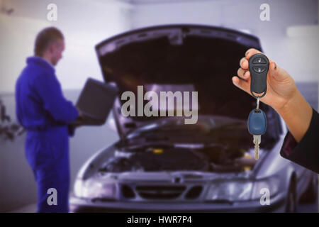 Woman holding key et petite voiture contre mechanic sur ordinateur à côté d'une voiture Banque D'Images