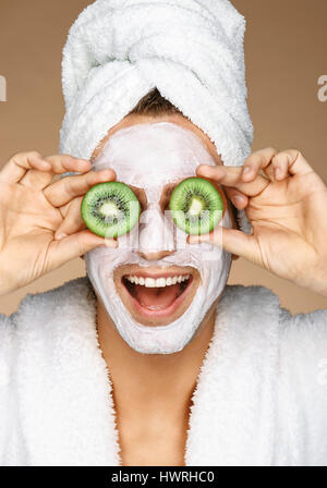 Jeune homme drôle avec masque facial et des morceaux de kiwis sur les yeux. Photo de grand homme recevant des soins spa. Beauté et Soins De La Peau concept Banque D'Images