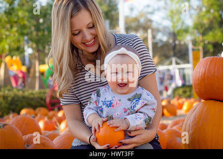 Portrait of happy baby girl holding pumpkin en position assise avec la mère à la cour au cours de l'Halloween Banque D'Images