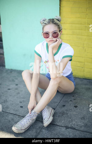 Portrait de femme à lunettes assis sur sentier contre mur Banque D'Images