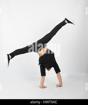 Jeune homme musclé breakdancer se tient sur ses mains. Il porte des vêtements noirs et fond blanc snapback . Banque D'Images