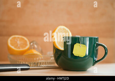 Tasse de thé au citron avec tranche de citron, sur un surfve en bois avec un citron centrifugeuse dans fond de bois. Banque D'Images