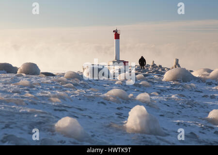 Un homme marche sur un quai congelé avec un phare sur une très froid matin. Oakvile, Ontario, Canada. Banque D'Images