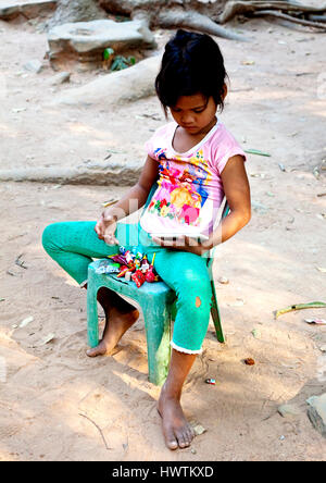 Jeune fille contrôler son téléphone intelligent tout en se reposant sur une chaise à Ta Phrom temple à Siem Reap au Cambodge Banque D'Images