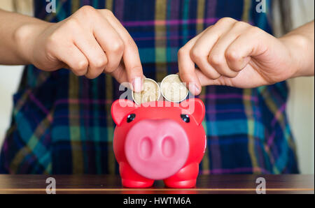 En plaçant des pièces de monnaie dans les mains de womans pink piggy bank Banque D'Images