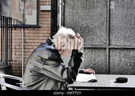 Man blouson de cuir assis dehors fumer et lire un journal Banque D'Images