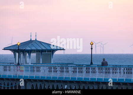 Une personne qui prend à la fois un matin tôt à pied le long de la jetée de Llandudno et le lever du soleil comme il se casse sur l'horizon à Llandudno, au Pays de Galles Banque D'Images