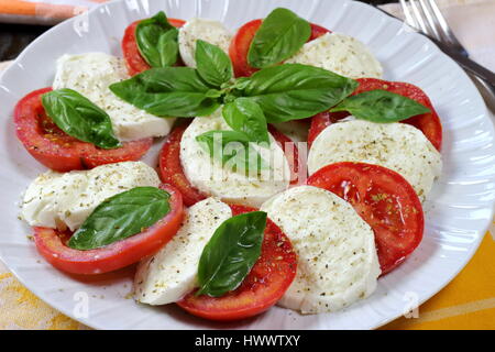 La tomate et mozzarella di buffala Caprese salade d'été close up avec la fourchette dans le fond et sur le dessus de basilic frais - recette de cuisine italienne servie dans un plat blanc Banque D'Images