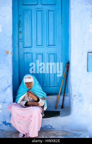 Chefchaouen, Maroc. Vieille Femme en costume traditionnel berbère assis sur sa porte. Banque D'Images