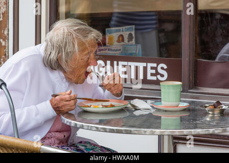 A senior woman de savourer son petit-déjeuner anglais complet alors qu'elle se trouve en dehors d'une cafétéria à Herne Bay Centre-ville. Banque D'Images