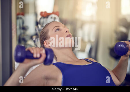 Jolie jeune femme travaillant dans une salle de sport avec une paire d'haltères dans une vue en gros dans un concept de santé et de remise en forme Banque D'Images