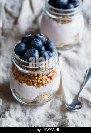 Close-up de muesli avec les baies fraîches, yogourt aux framboises et à la banane dans des bocaux en verre sur une serviette beige lin rustique Banque D'Images
