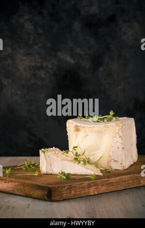 Photo verticale inhabituelle avec le camembert. En forme de cube de fromage avec le cresson sur vintage planche à découper avec la partie coupée. Plaque de porte noire est utiliser Banque D'Images