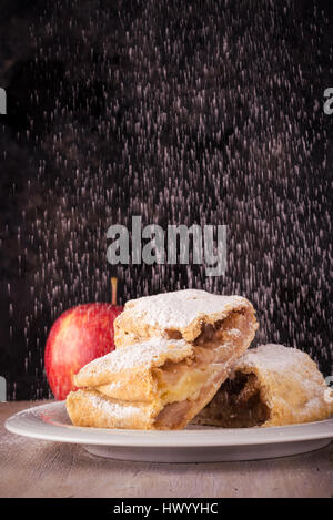Photo verticale avec deux tranches de strudel et seule pomme rouge. Deux portions sont couverts par du sucre en poudre qui est renversé par le haut sur une soucoupe blanche. Pl Banque D'Images