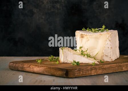 Photo horizontale avec le camembert. En forme de cube de fromage avec le cresson sur vintage planche à découper avec la partie coupée. Plaque de porte noire est u Banque D'Images