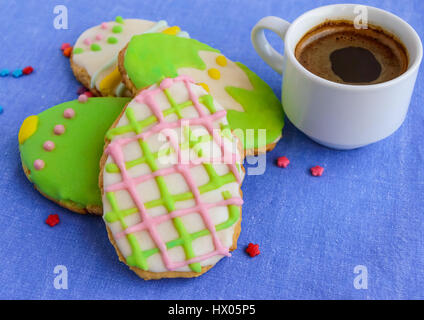 Maison de vacances Gingerbread Cookie dans la forme d'un oeuf, avec glacis multicolores sur une serviette bleue et tasse de café. Banque D'Images