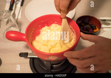 Préparation de la fondue. Faire fondre le fromage dans un pot rouge coquelon Banque D'Images
