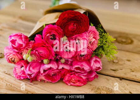 Bouquet de roses et un drak plusieurs renoncules rouge enveloppé dans du papier craft lying on wooden table rustique présentation paysage Banque D'Images