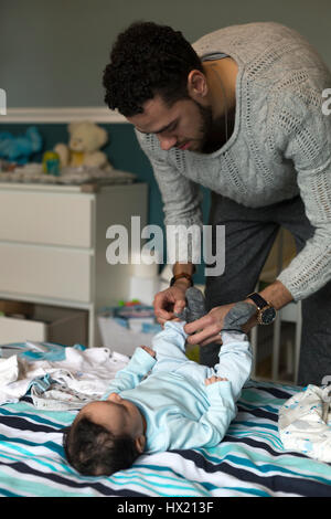 Jeune père met quelques chaussettes sur son fils, encore bébé, qui est allongé sur le lit des parents. Banque D'Images