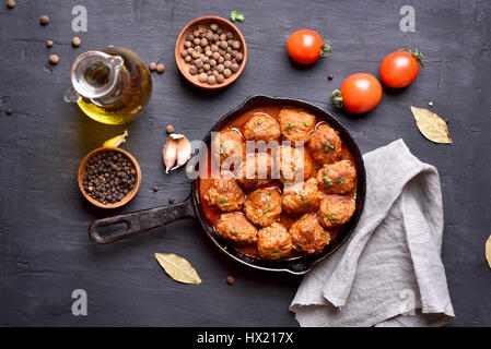 Boulettes de viande avec sauce de tomate dans une poêle à frire sur fond sombre, vue du dessus Banque D'Images