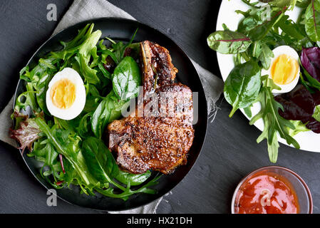 Salade verte avec des œufs et du porc bifteck sur le plaque sur fond sombre, vue du dessus Banque D'Images