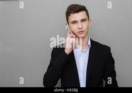 Closeup portrait, beau jeune homme d'affaires, heureux guy, en gilet, using cell phone, smiling, avoir une conversation agréable, isolé sur fond noir gris. Les émotions humaines, d'expression Banque D'Images