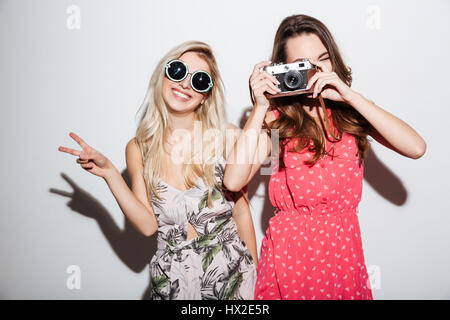 Deux femmes élégantes souriant faisant des photos avec appareil photo rétro isolé sur fond blanc Banque D'Images