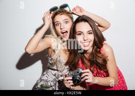 Deux jeunes femmes heureux de faire des photos avec l'appareil photo rétro isolé sur fond blanc Banque D'Images