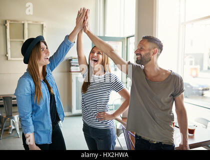 Young smiling trendy de collègues faisant des gestes à la lumière high five bureau spacieux. Banque D'Images