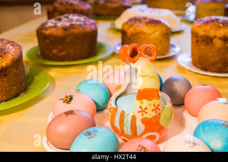 La cuisine de Pâques. Close-up plaque avec les oeufs colorés sur fond jaune sur la nappe de plusieurs gâteaux de Pâques. Banque D'Images