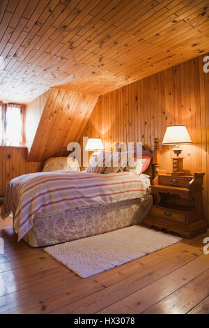 Raised Single lit dans la chambre avec des murs en pin noueux dans Canadiana log home intérieur éclairé par la lumière d'or chaud Banque D'Images