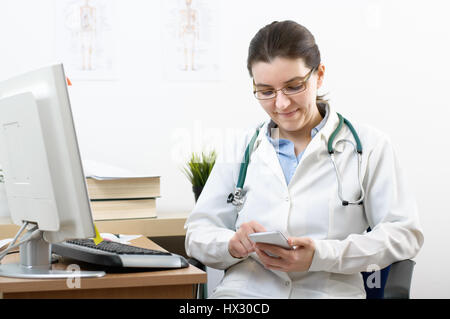 Smiling female doctor using smartphone dans son bureau Banque D'Images