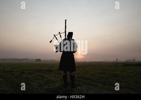 Un musicien joue de la cornemuse dans les champs au coucher du soleil. Banque D'Images