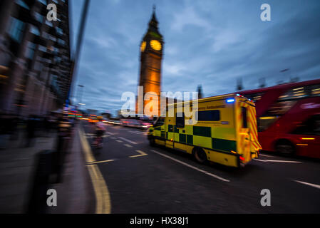 Une ambulance des déplacements à grande vitesse au crépuscule avec feux bleus clignoter passé les chambres du Parlement à Londres en passant un bus rouge et Big Ben Banque D'Images