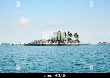 Formation rocheuse naturelle en mer avec des palmiers et de la végétation verte sur le dessus à Belitung Island dans l'après-midi et un phare blanc à l'arrière-plan Banque D'Images