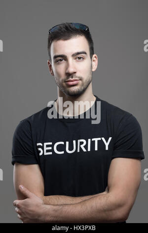 Garde de sécurité Cool fit en chemise noire avec bras croisés en regardant la caméra. Portrait de l'atmosphère contrastée gris sur fond de studio. Banque D'Images