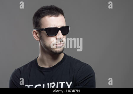 Agent de sécurité difficiles macho portant des lunettes de soleil à la voiture à copyspace. Portrait de l'atmosphère contrastée gris sur fond de studio. Banque D'Images